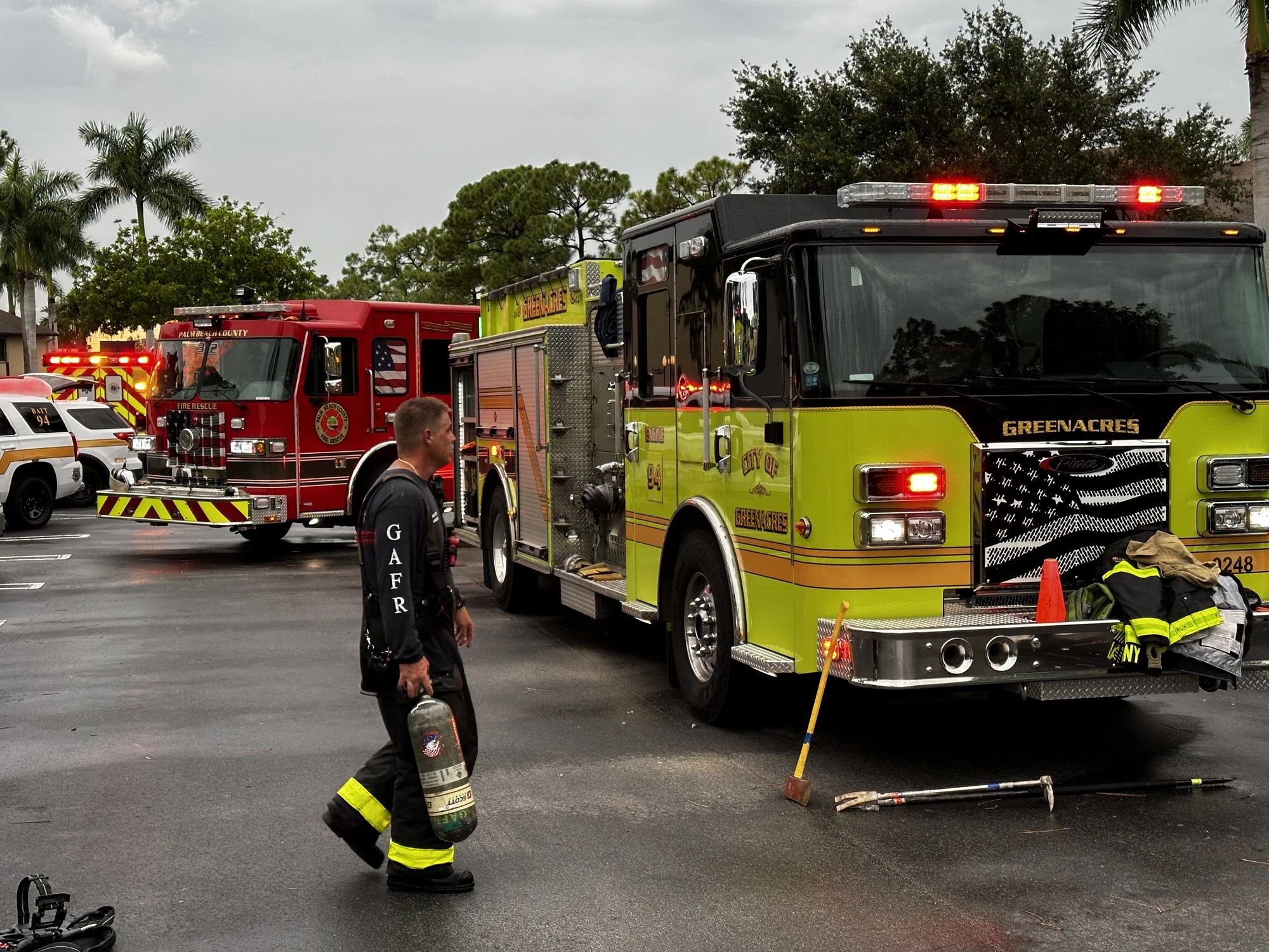 A Greenacres firefighter carrying an air cylinder past Greenacres Fire Rescue Engine 94, with Palm Beach County Fire Rescue apparatus behind