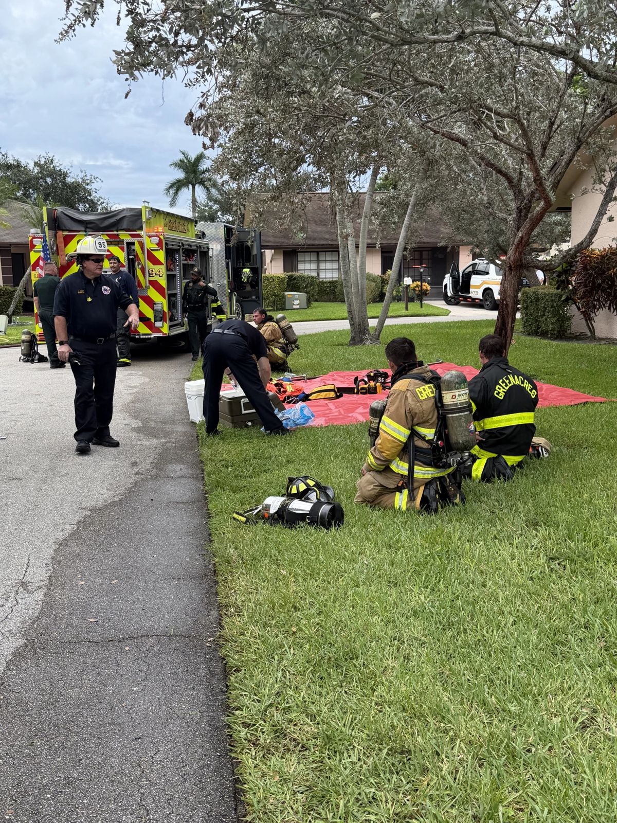 Greenacres Fire Rescue firefighters with equipment staged on a lawn beside their engine
